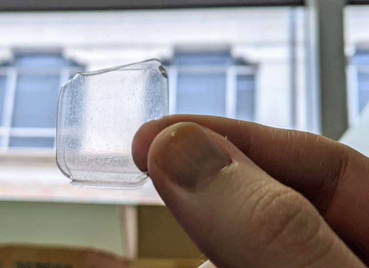 Thumb and forefinger holding postage stamp-sized piece of clear plastic film