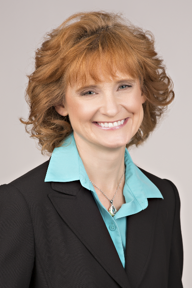 headshot of woman with short red hair wearing a black suit and green blouse